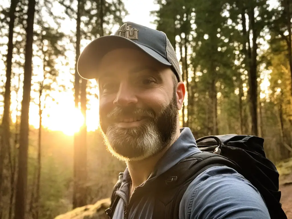 About the Website Designer Kyle standing in the woods wtih the sunset behind him.